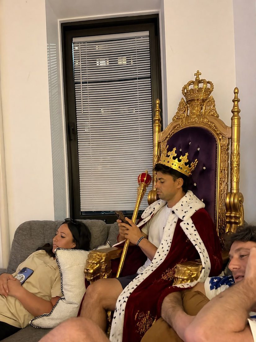 Someone in a crown and robe sitting on a gold throne in the apartment living room